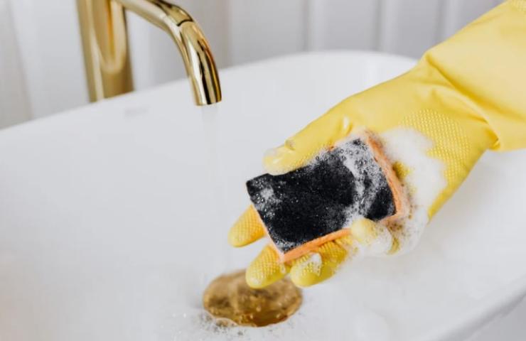 persona deterge il lavandino del bagno con una spugnetta