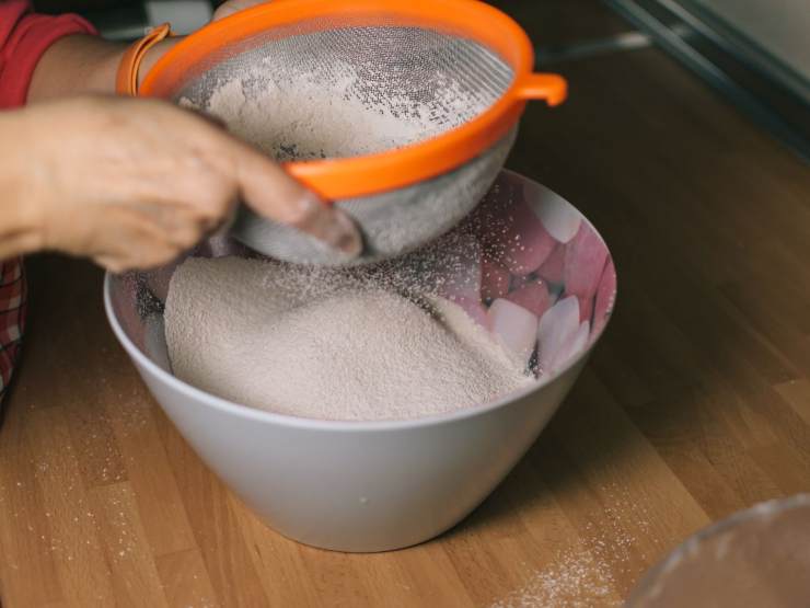 persona che setaccia farina in ciotola
