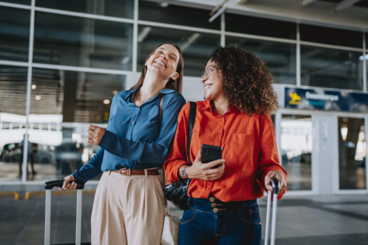 due donne con le valigie che sorridono fuori dall'aeroporto