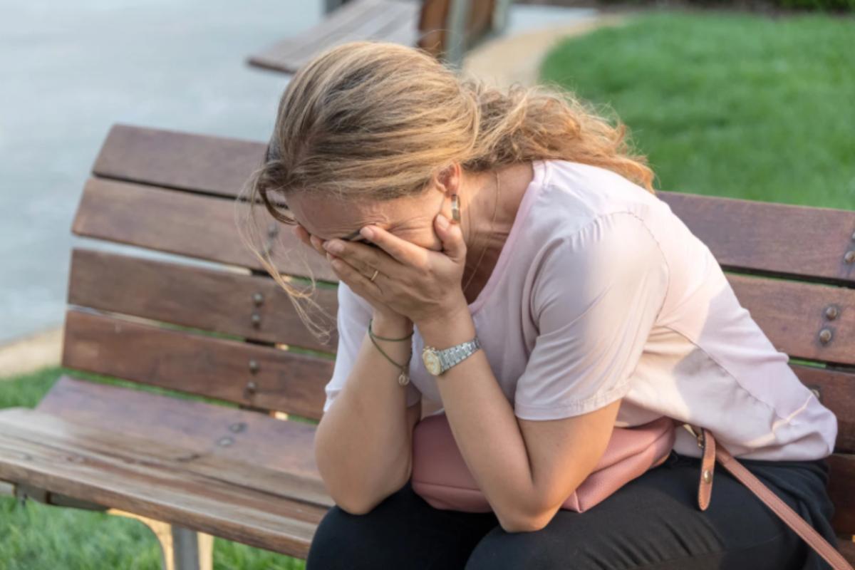 donna disperata con le mani in faccia seduta su una panchina