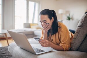 donna piange di fronte a pc e con carta di credito in mano