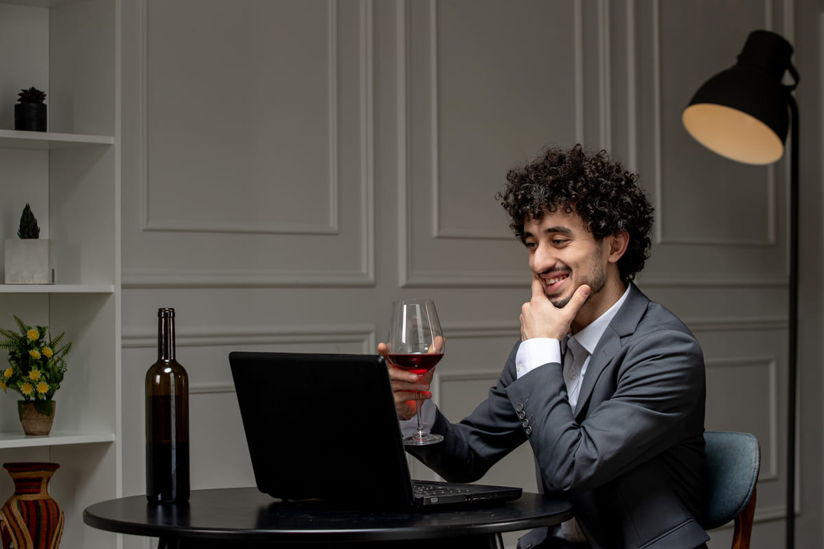 Uomo con bicchiere di vino in mano che guarda il laptop